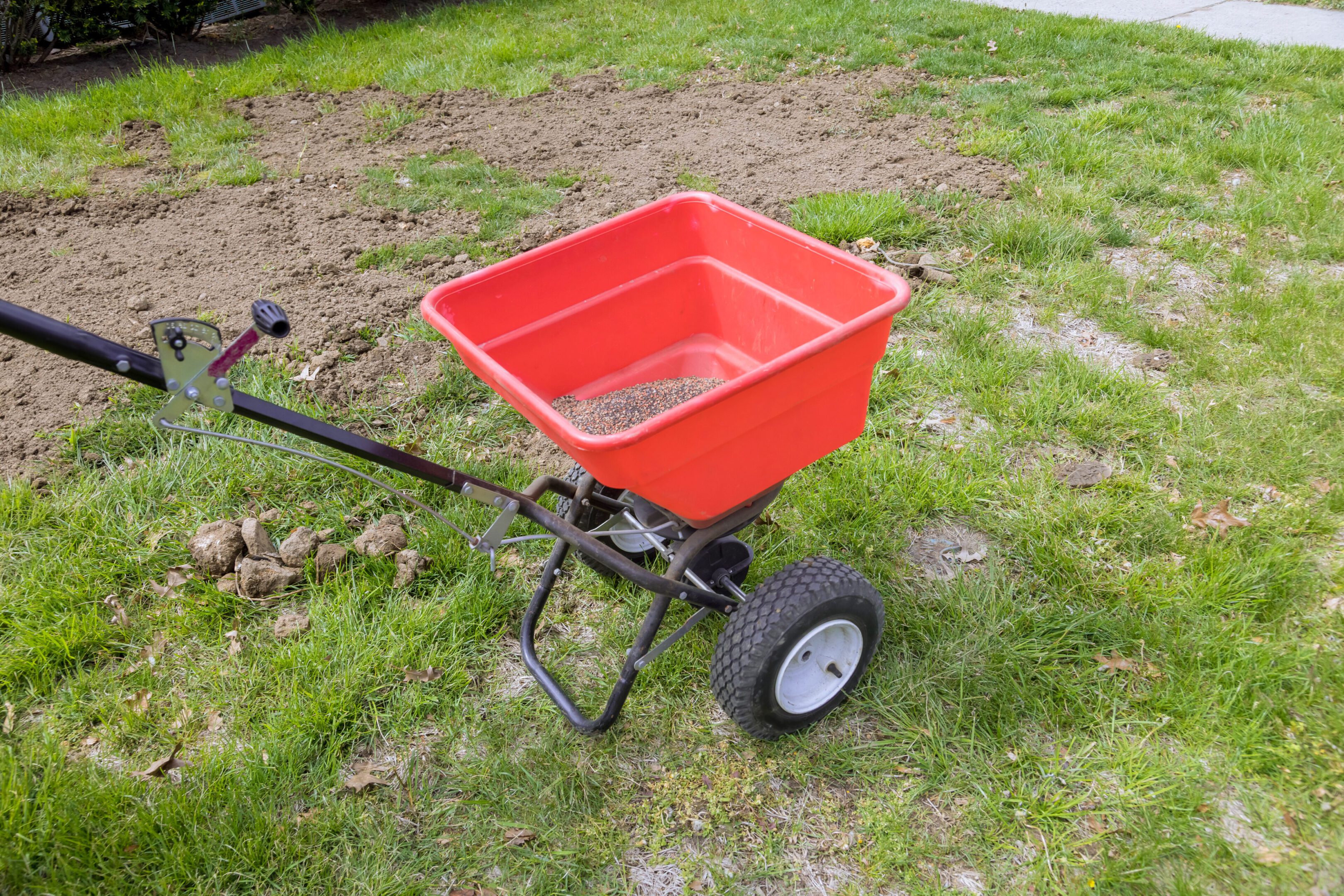 A red garden spreader on grass for fertilizer or seed spreading.