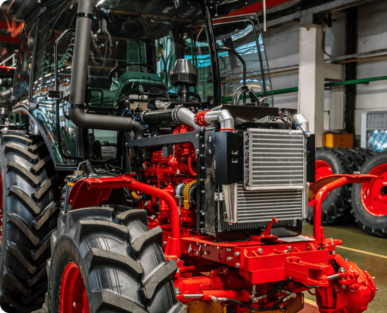A close-up of a red tractor's engine and front wheel inside a workshop.