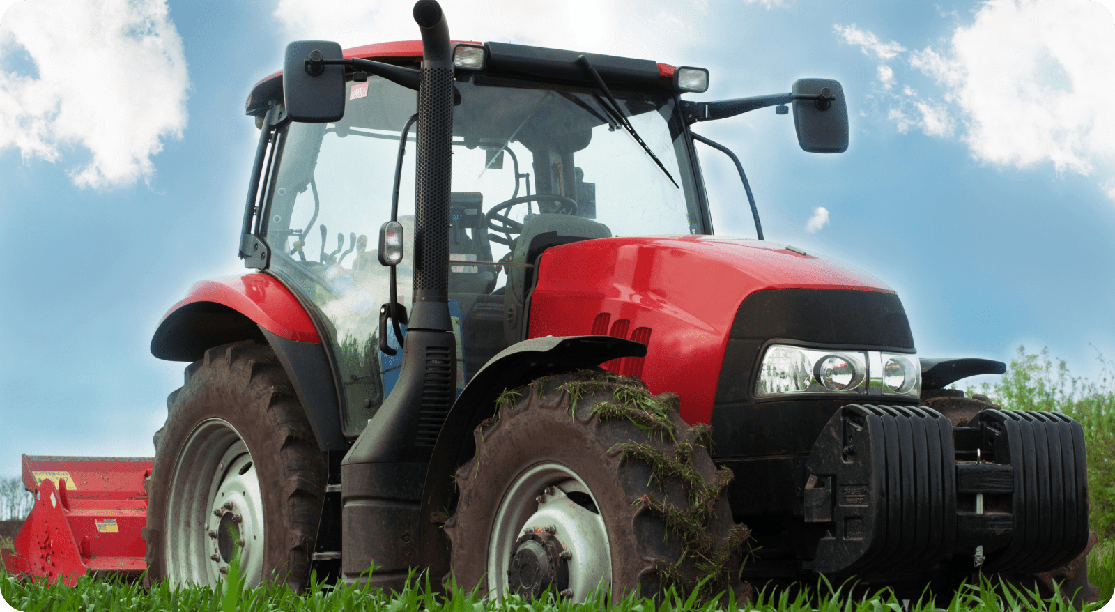 Red tractor parked on green grass under blue sky.